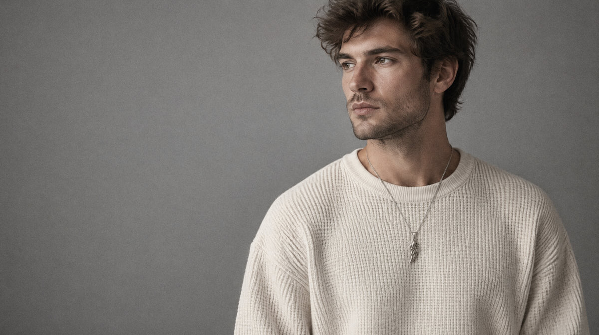 A man in a cream knit wearing a silver wing pendant