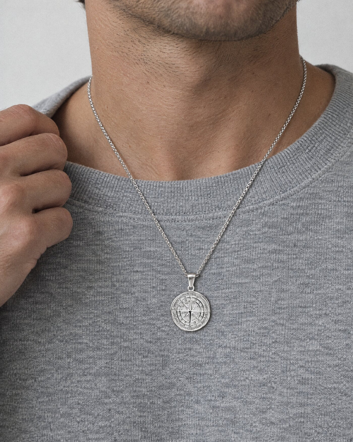 A silver compass pendant worn over a grey sweatshirt