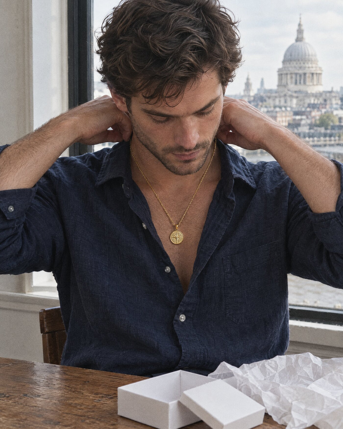 A man fastening a gold compass pendant beside an opened gift box
